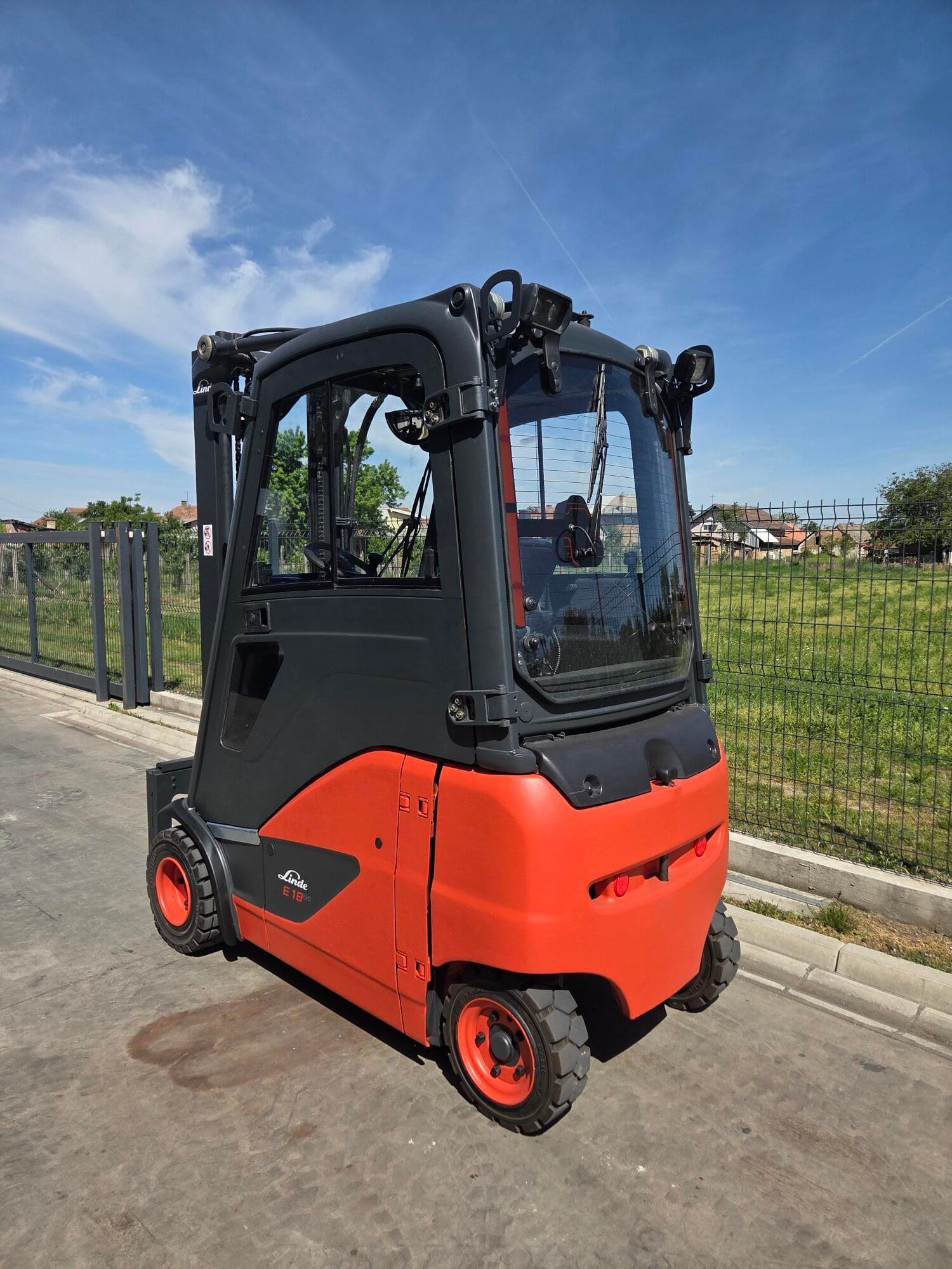 E18ph-103 | Jović Viljuškari Black and orange Linde forklift with enclosed cab front wheel visible outdoors by a metal fence under a blue sky Model E18