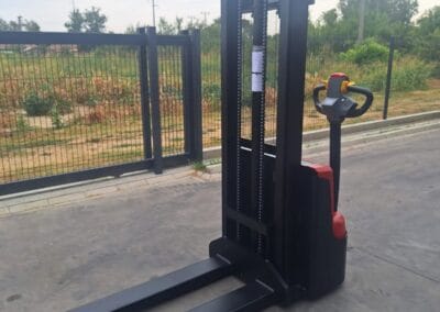 staxx-ws15h-2 | Jović Viljuškari Electric pallet stacker with long forks parked on a concrete surface outdoors near a fence.